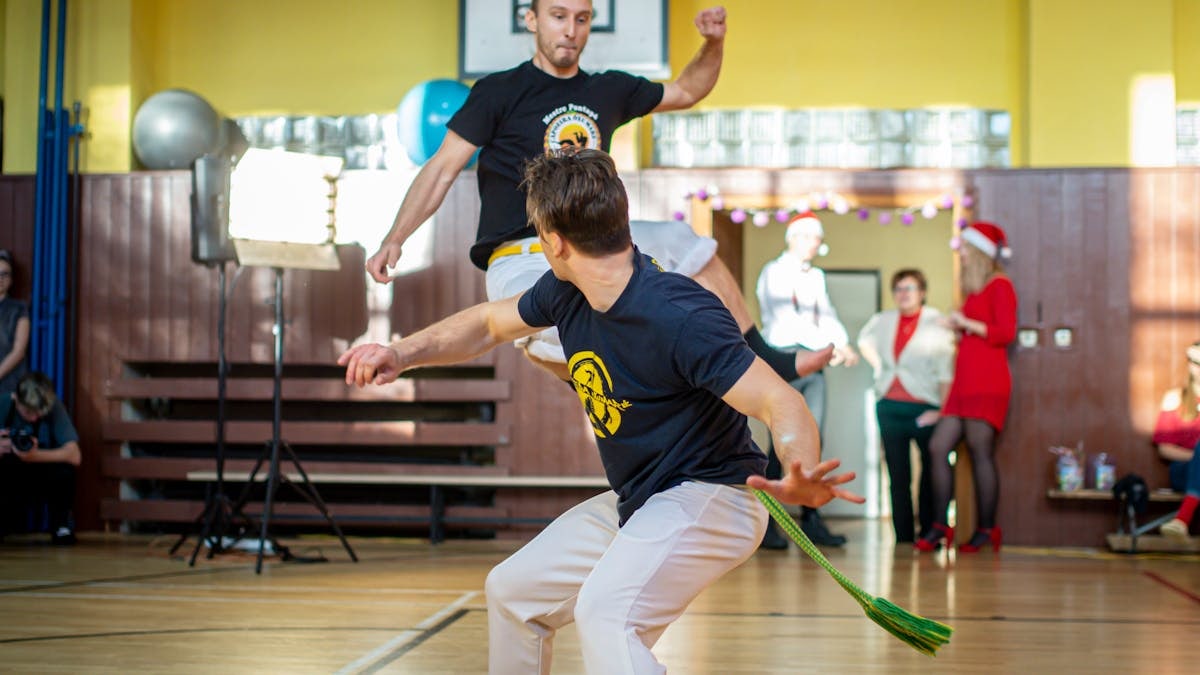Energetic capoeira performance indoors with audience during daytime.